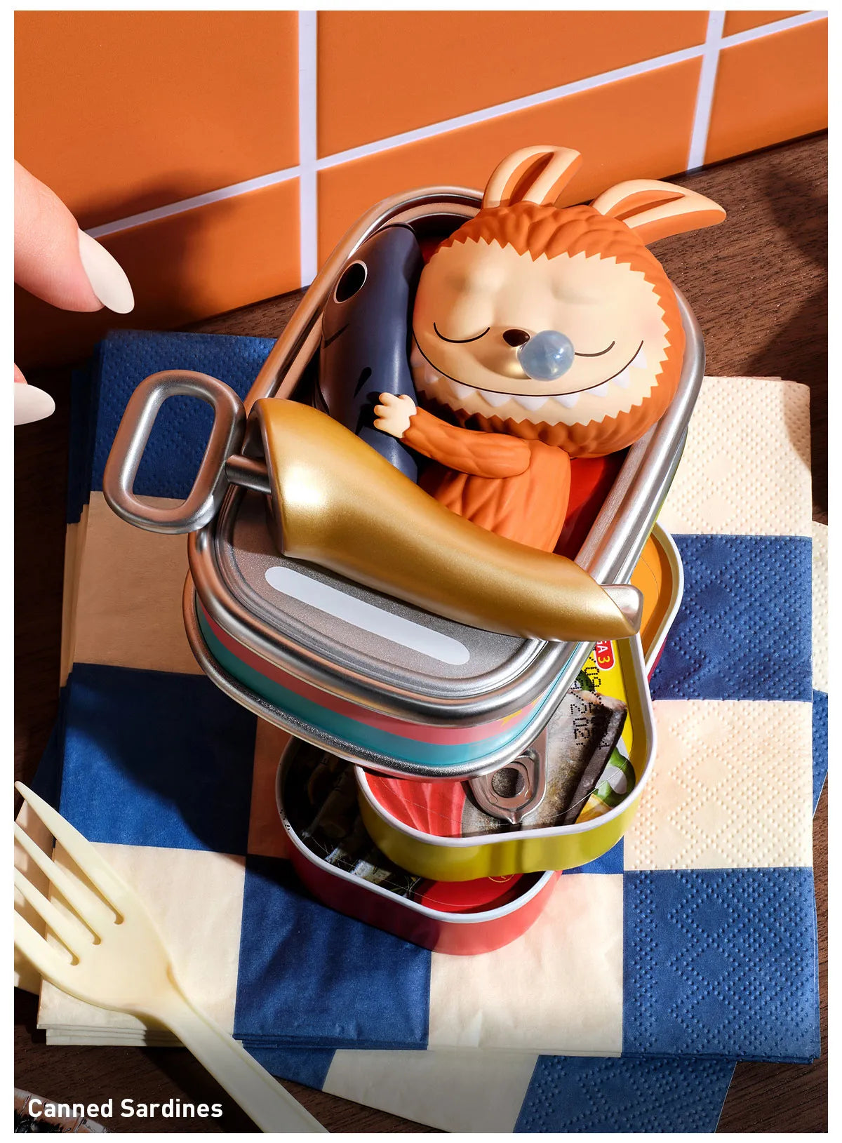 Canned sardines with a decorative lid featuring a cartoon fox character on a checkered tablecloth. Collectible Labubu pop mart toys