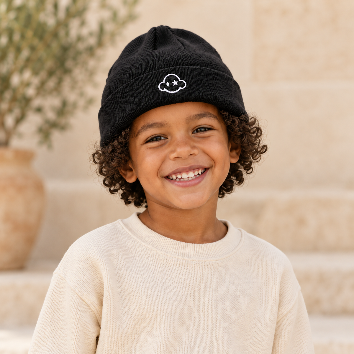 Child wearing DREAM BIG black kids beanie — front cloud logo