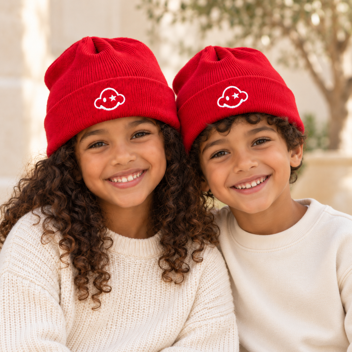 Girl and boy wearing red DREAM BIG kids beanies with white cloud embroidery