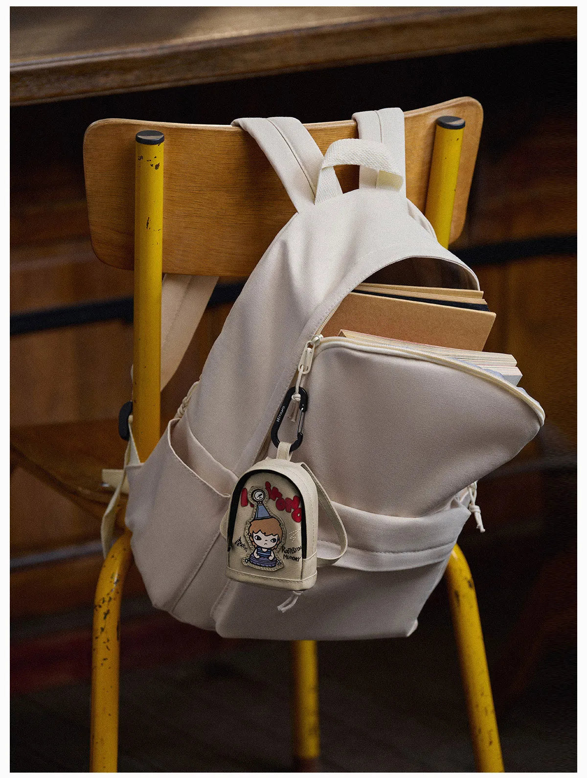 Beige backpack with a small character pouch on a yellow chair  Collectible Labubu pop mart toys Hirono