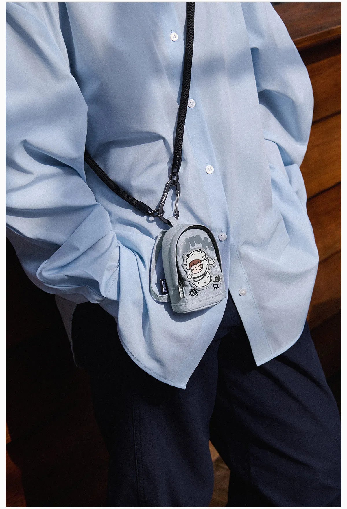 Person wearing a light blue shirt with a small gray bag featuring a cartoon character on their shoulder.  Collectible Labubu pop mart toys Hirono