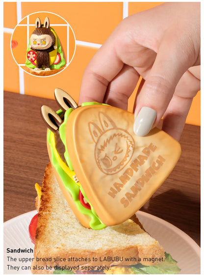 Handmade cookie shaped like a sandwich with a hand holding it, on a wooden surface.  Collectible Labubu pop mart toys