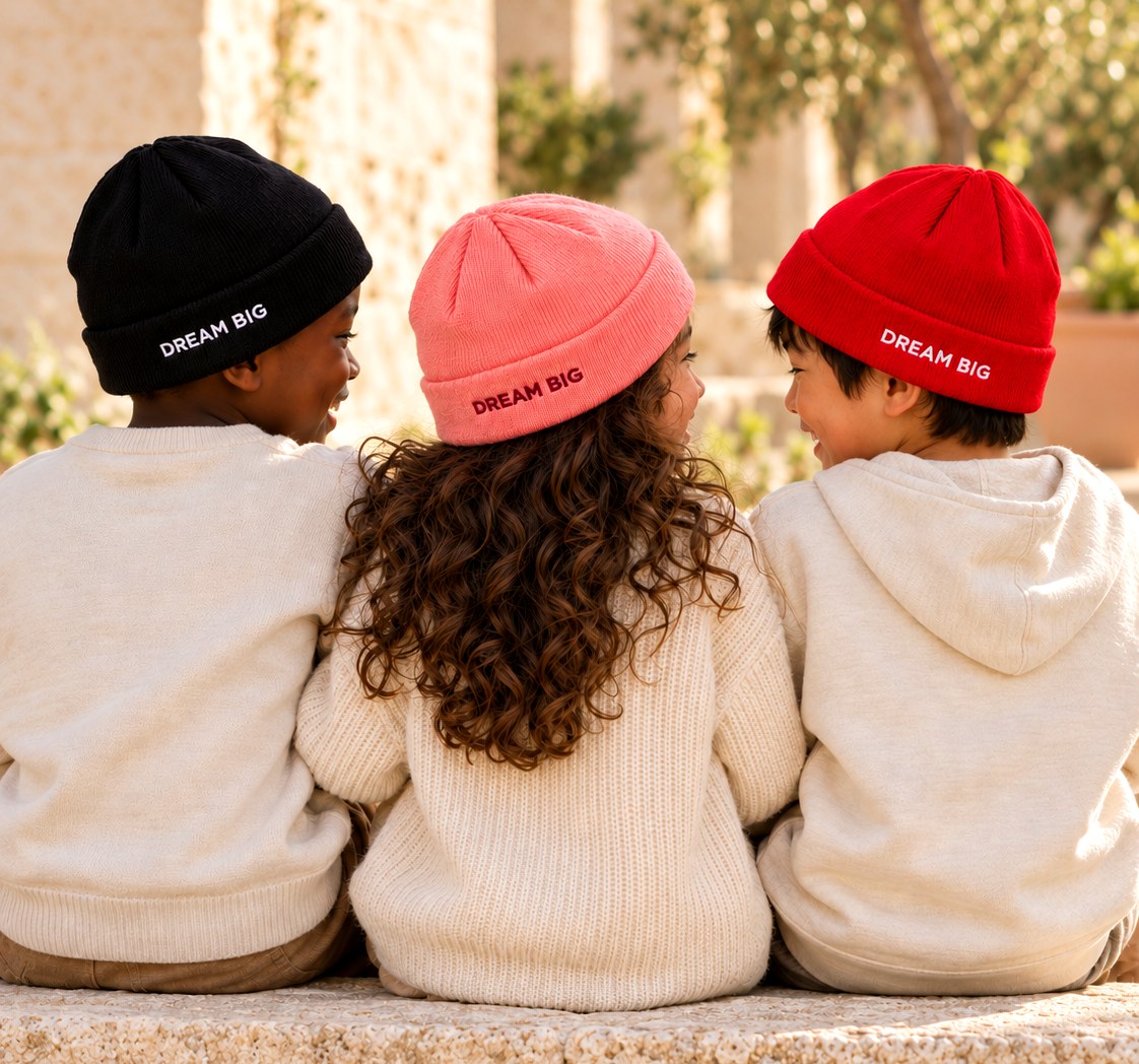 Three children from behind wearing DREAM BIG beanies in black, pink and red
